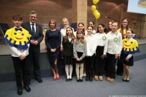 Uroczystość wręczenia Orderu Uśmiechu. Laureatka pozuje do zdjęcia z dziećmi i kapitułą konkursu. W tle żółte balony z uśmiechami.