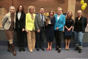 Uroczystość wręczenia Orderu Uśmiechu. Laureatka, trzymająca psa na rękach, pozuje do zdjęcia z pracownikami uczelni. W tle po prawej żółte balony z uśmiechami.