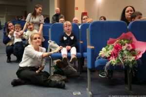 Uroczystość wręczenia Orderu Uśmiechu. Widownia. Na fotelach mamy z dziećmi. Na pierwszym fotelu bukiet kwiatów.