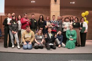 Uroczystość wręczenia Orderu Uśmiechu. Laureatka, trzymająca kwiaty, pozuje do zdjęcia z młodzieżą. W tle po prawej żółte balony z uśmiechami.