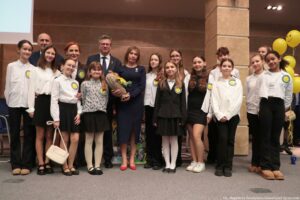 Uroczystość wręczenia Orderu Uśmiechu. Laureatka pozuje do zdjęcia z dziećmi i kapitułą konkursu. W tle po prawej żółte balony z uśmiechami.