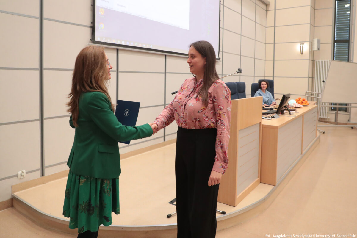 Perły Instytutu Ekonomii i Finansów 2025. Po prawej wyróżniona naukowczyni odbierająca teczkę, po lewej dyrektorka Instytutu. W tle mównica.