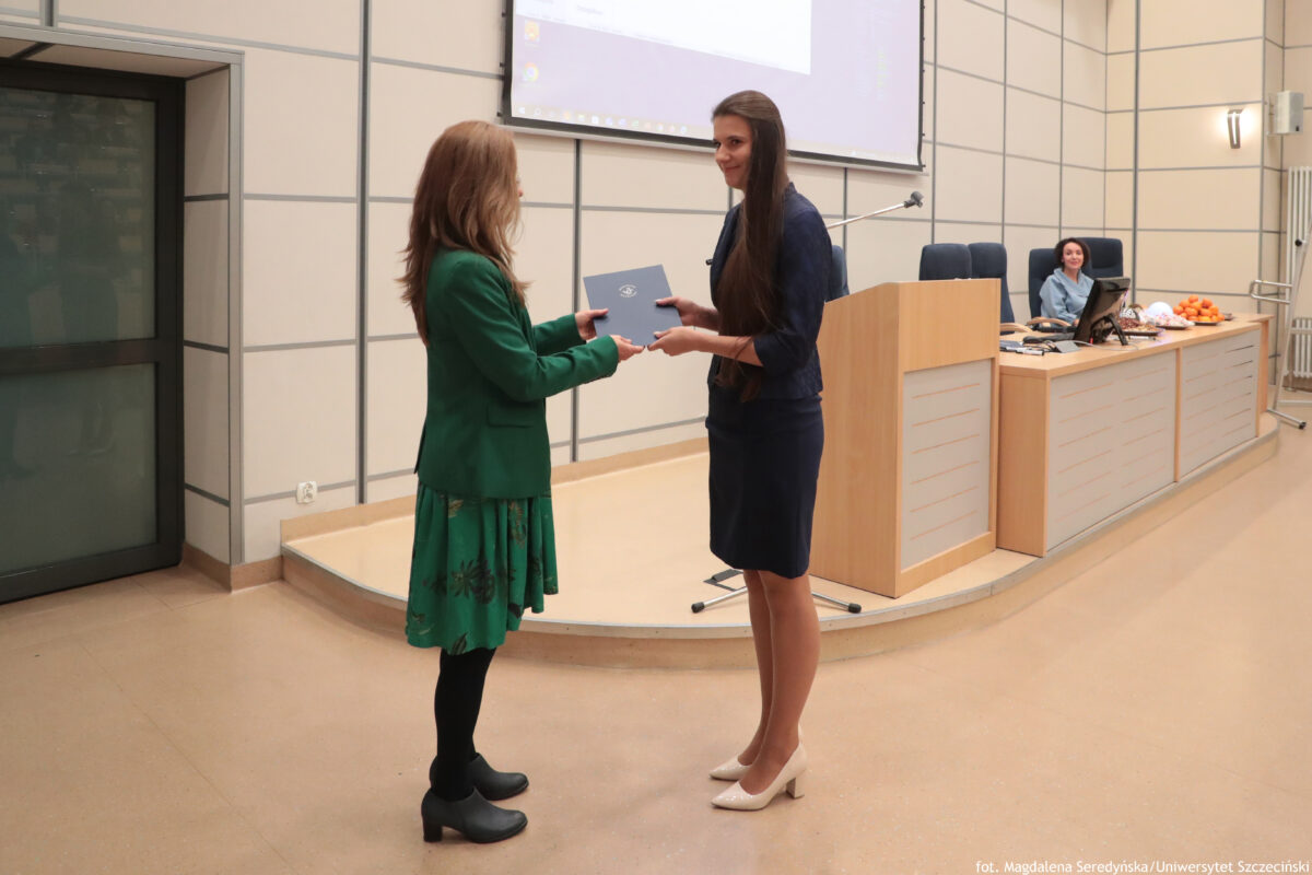 Perły Instytutu Ekonomii i Finansów 2025. Po prawej wyróżniona naukowczyni odbierająca teczkę, po lewej dyrektorka Instytutu. W tle mównica.