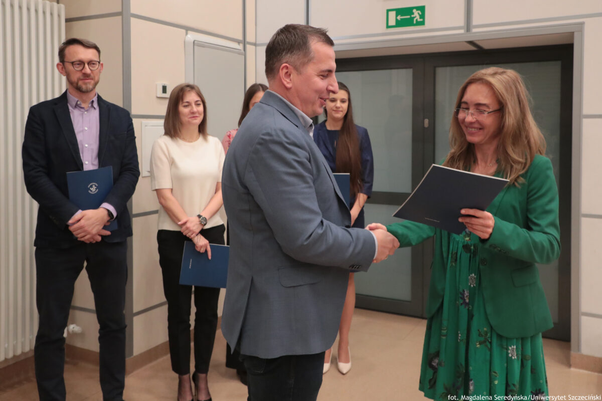 Perły Instytutu Ekonomii i Finansów 2025. Po lewej wyróżniony naukowiec odbierający teczkę, po prawej dyrektorka Instytutu. W tle czworo innych wyróżnionych.