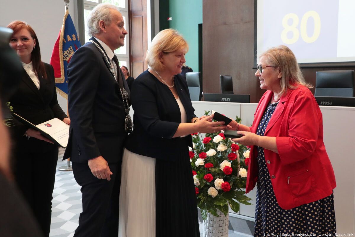 Prof. dr hab. Maria Czerepaniak-Walczak z Uniwersytetu Szczecińskiego odbierająca Medal za Zasługi dla Miasta Szczecina. Na dole stojące na podłodze biało-czerwone goździki umieszczone w białym koszu.