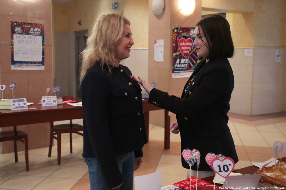 Prorektor ds. studenckich Uniwersytetu Szczecińskiego dostaje naklejkę czerwonego serduszka za wrzucenie banknotu do puszki Wielkiej Orkiestry Świątecznej Pomocy podczas uczelnianego kiermaszu charytatywnego.