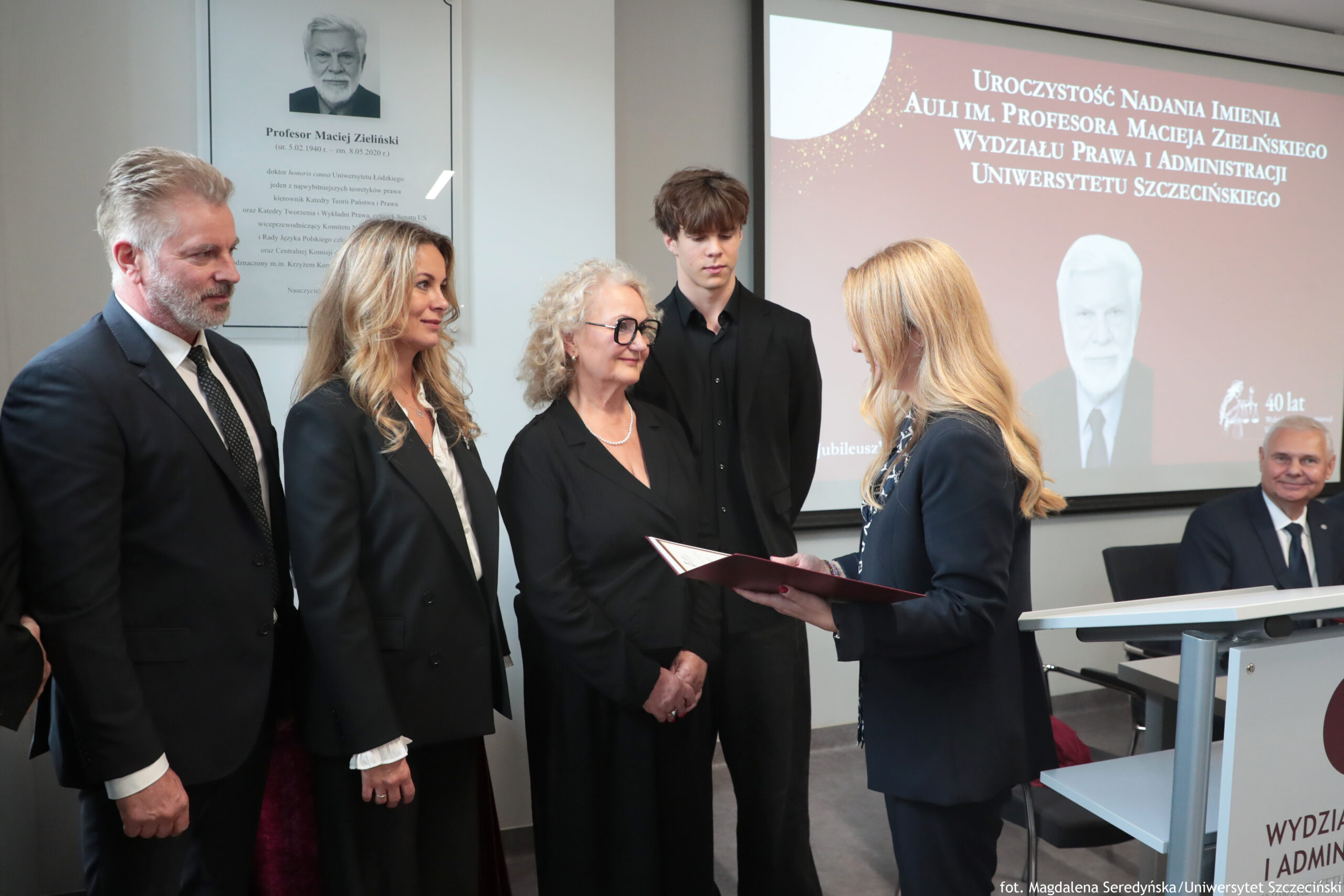 Uroczystość nadania auli im. Profesora Macieja Zielińskiego – Wydział Prawa i Administracji Uniwersytetu Szczecińskiego. Dziekan Wydziału dr hab. Ewelina Cała-Wacinkiewicz, prof. US (po prawej, bokiem), 4-osobowa rodzina profesora (bokiem po lewej). W tle odsłonięta tablica.